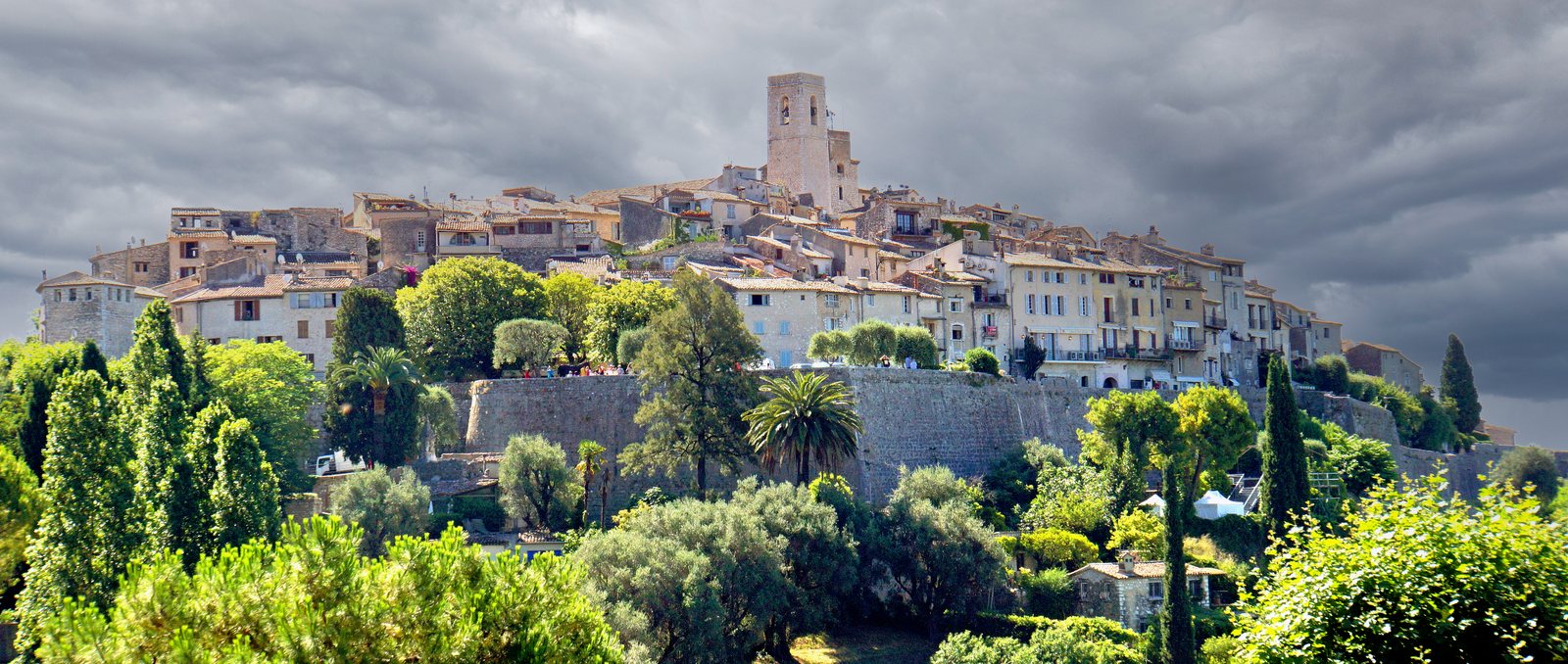 The walled village of Saint-Paul-de-Vence on its wooded ridge, stone houses and the bell tower rising above the ramparts under a heavy sky
