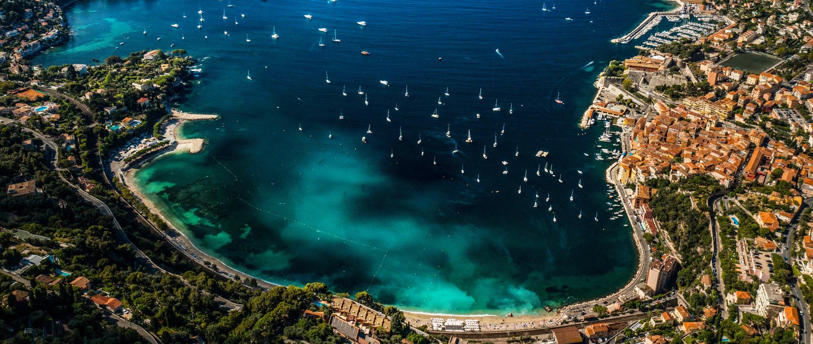 Aerial view of the bay of Villefranche-sur-Mer with yachts at anchor, the old town and Citadelle on the right and Plage des Marini&egrave;res curving along the shore